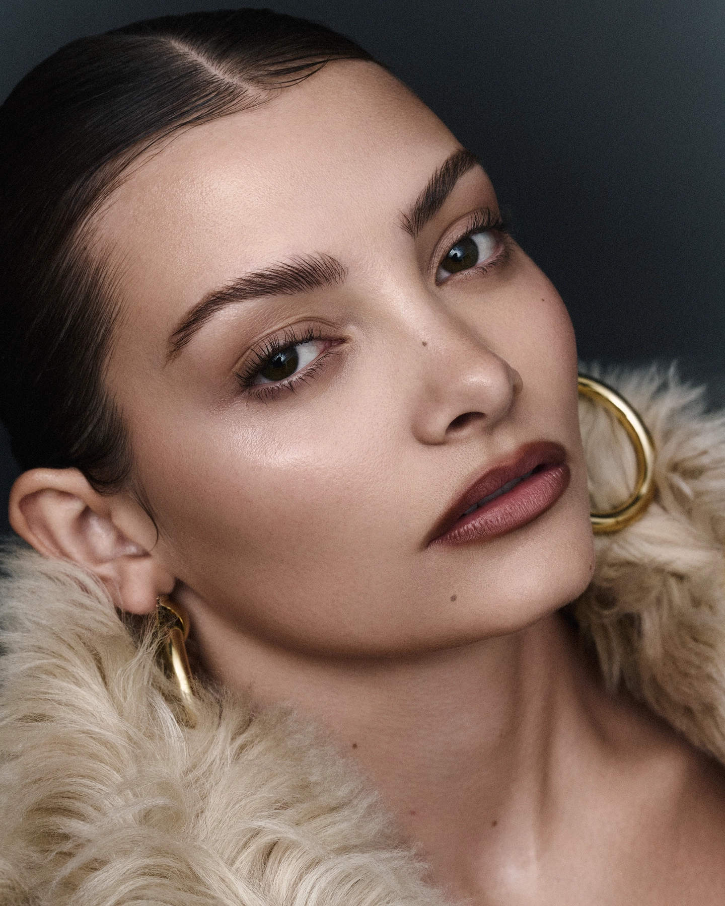 Alice L beauty close-up with glowing skin, gold hoop earrings and fur collar for Sicky Magazine, styled by Olof Runmarker, makeup by Denise Löfstrand