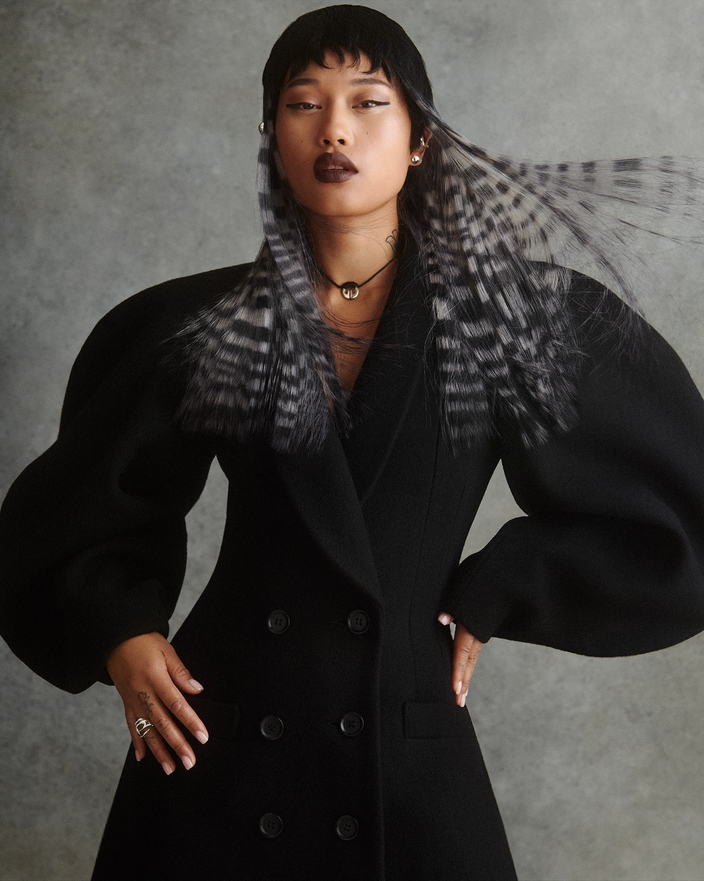 Elyse in black balloon-sleeve coat with feathered collar against textured backdrop for Vogue Philippines, makeup by Mary-Jane Gotidoc, hair by Michael Kent, styled by Carlos Mangubat