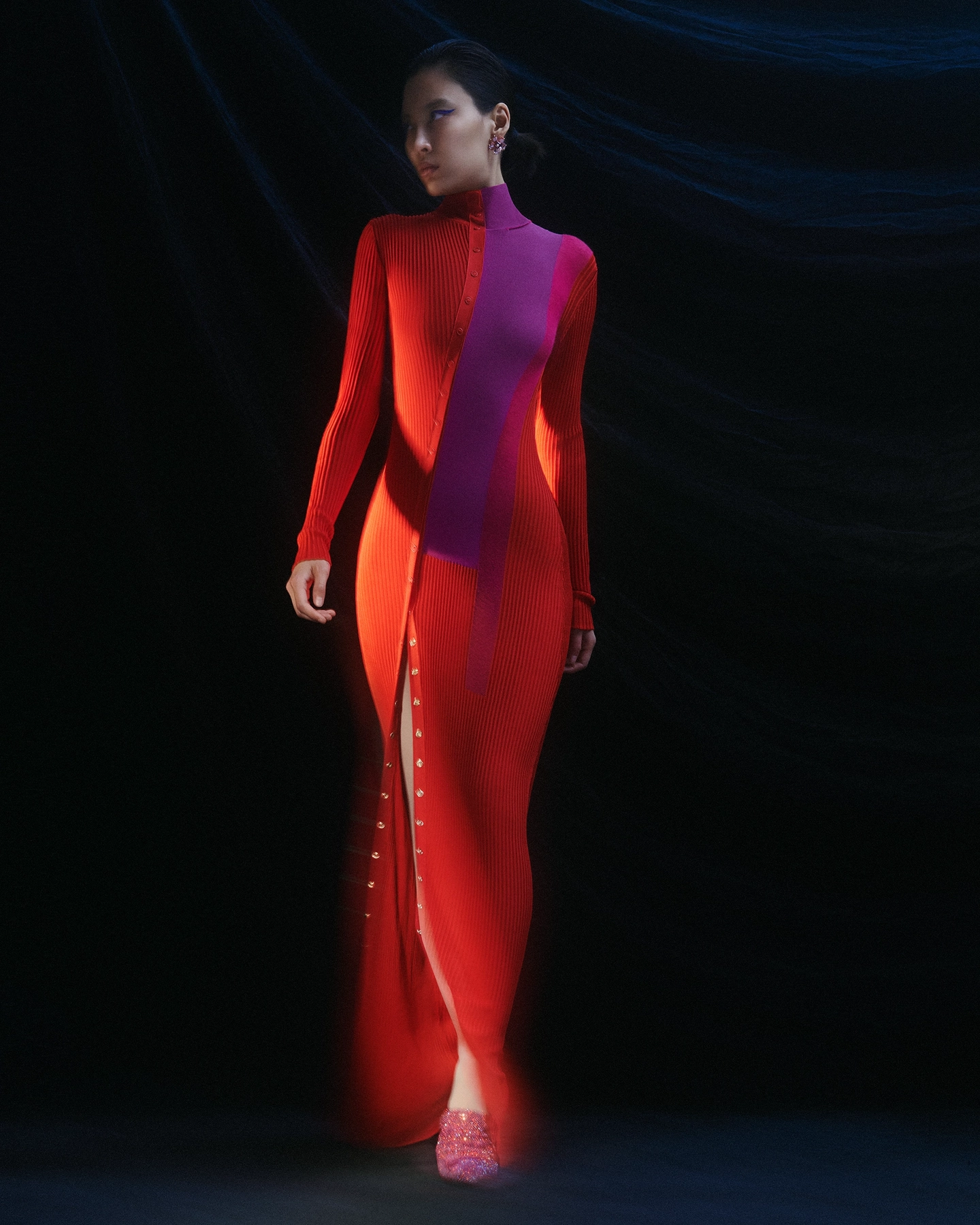 Model in vibrant red-orange and magenta ribbed column dress against dark background with light trails for 5 Eleven Magazine, styled by Joanne Kennedy, makeup by Adam De Cruz