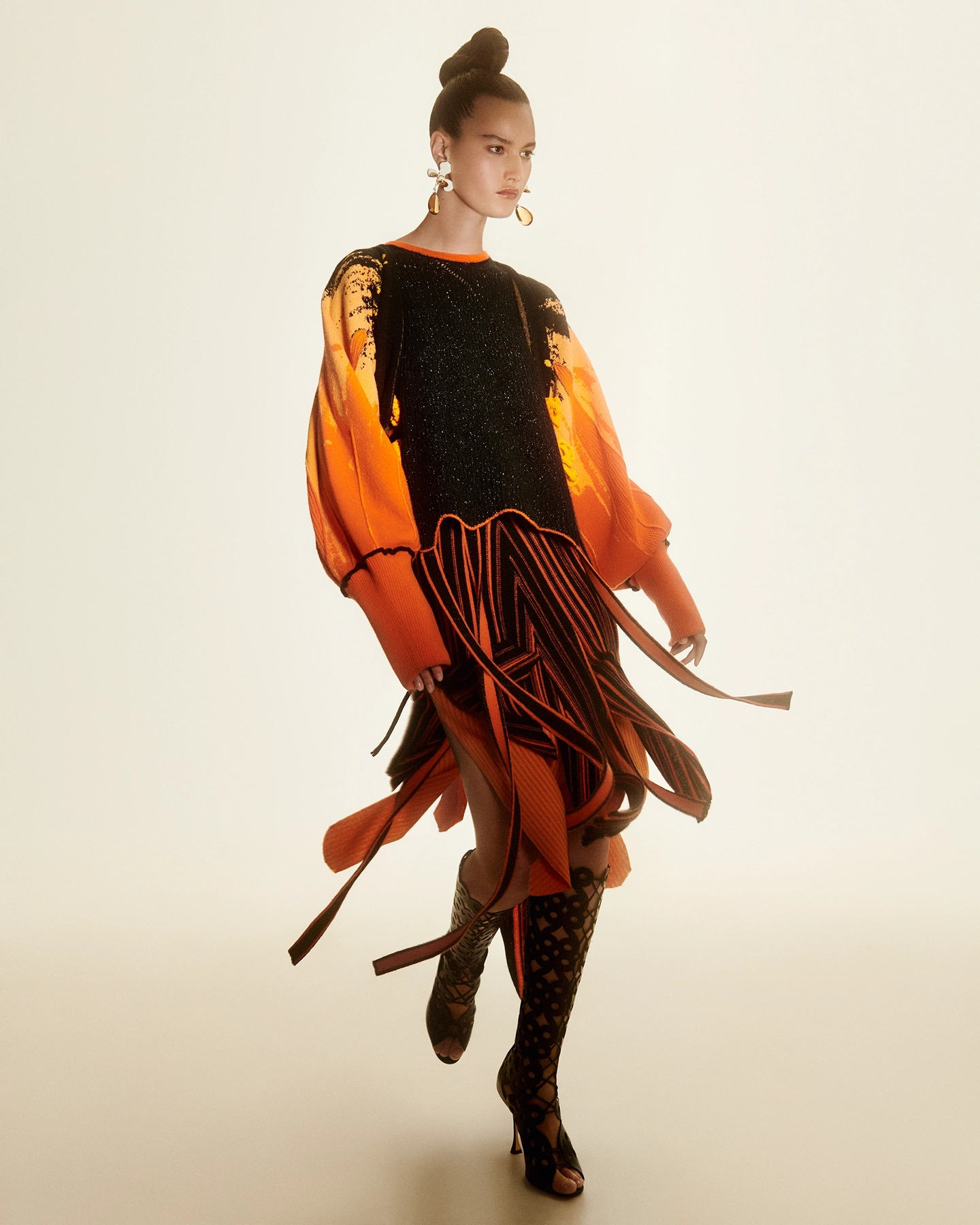 Model walking in orange and black layered fringe ensemble with patterned boots for Harpers Bazaar Arabia