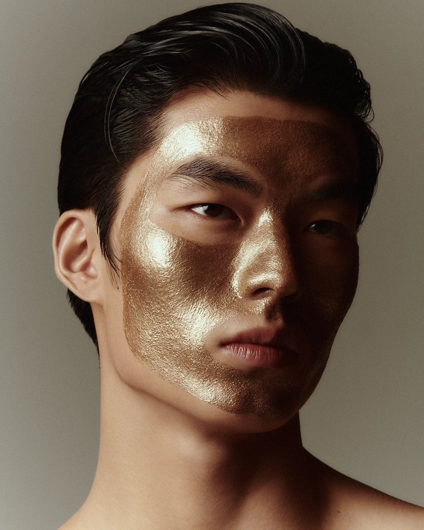 Nokal with metallic gold leaf covering half the face in warm studio light for Numero Netherlands in collaboration with A.D.C skincare