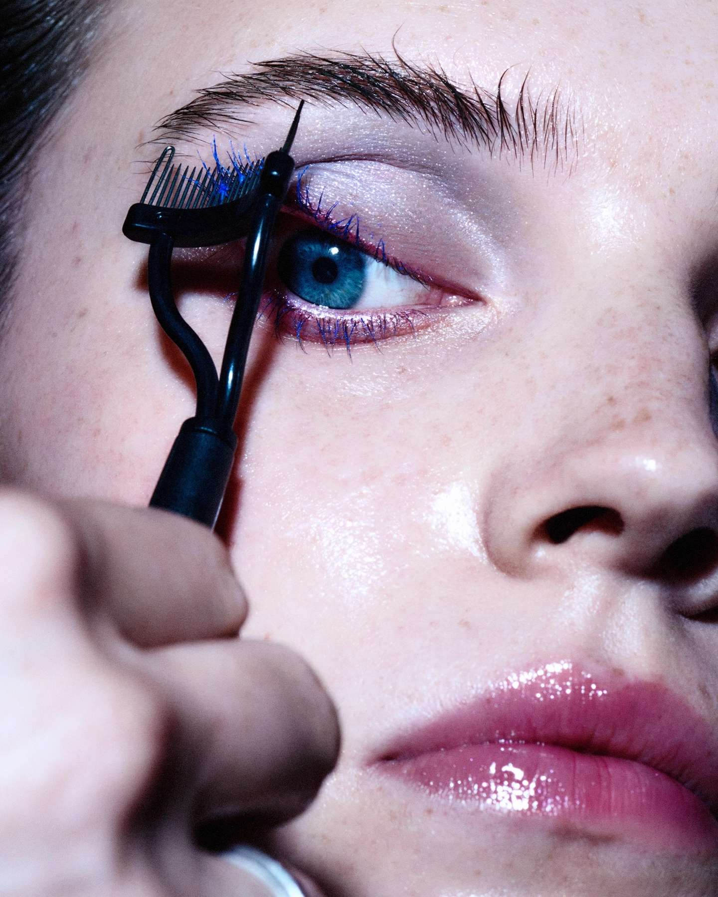 Close-up of eye with lash comb tool and blue-tinted mascara for Sicky Magazine, makeup by Jeanette Gjerde Olsen