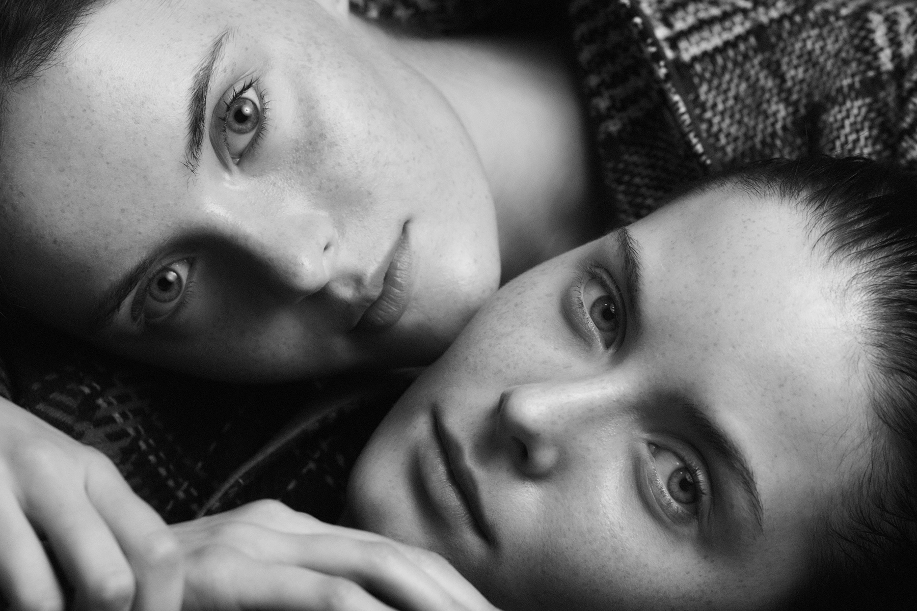 Black and white intimate portrait of twin models lying side by side wrapped in knitwear